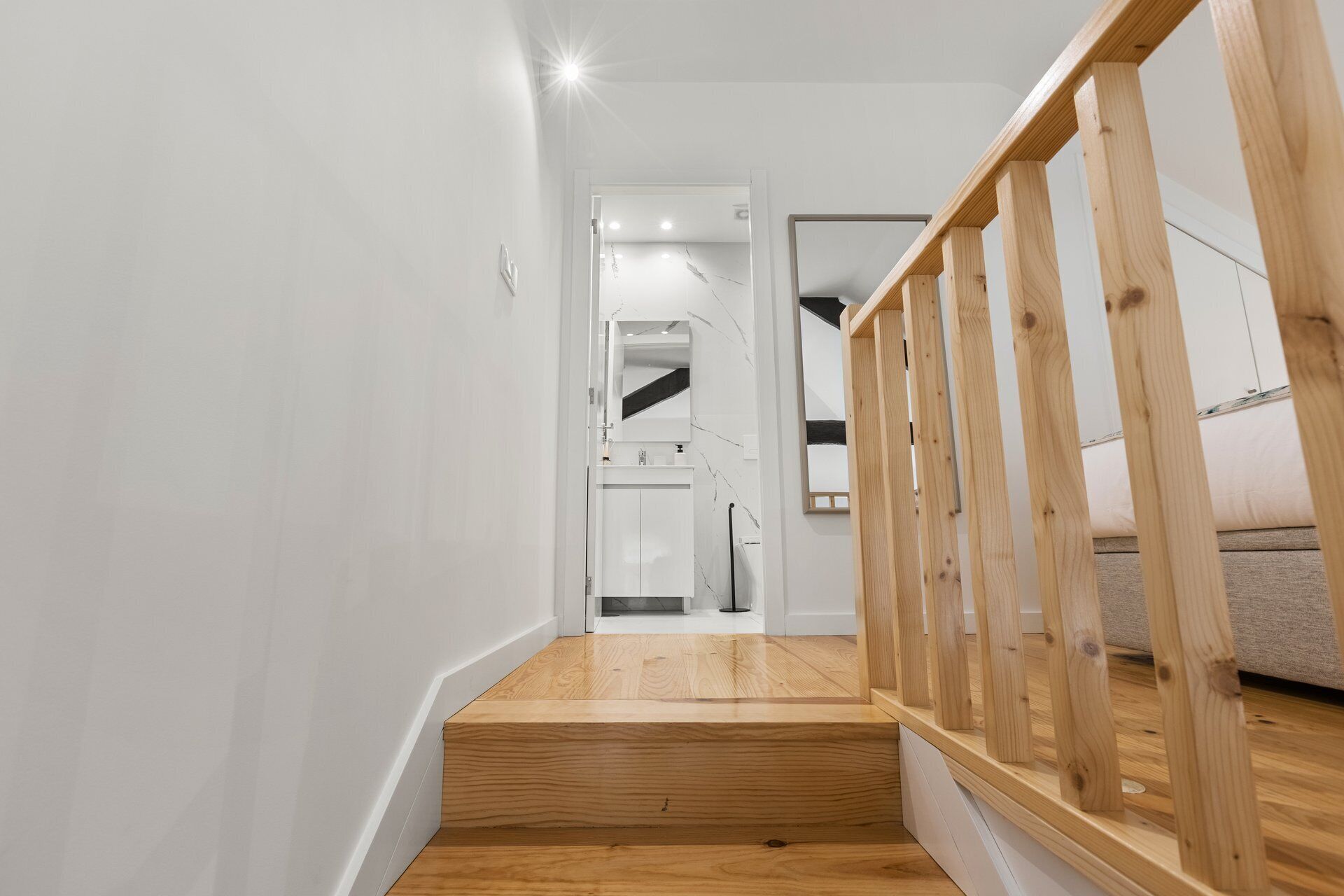 A staircase with wooden railings leading to a bathroom with a white sink and mirror.