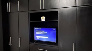 Una habitación con un armario negro, un televisor de pantalla plana montado en la pared y suelo de baldosas.