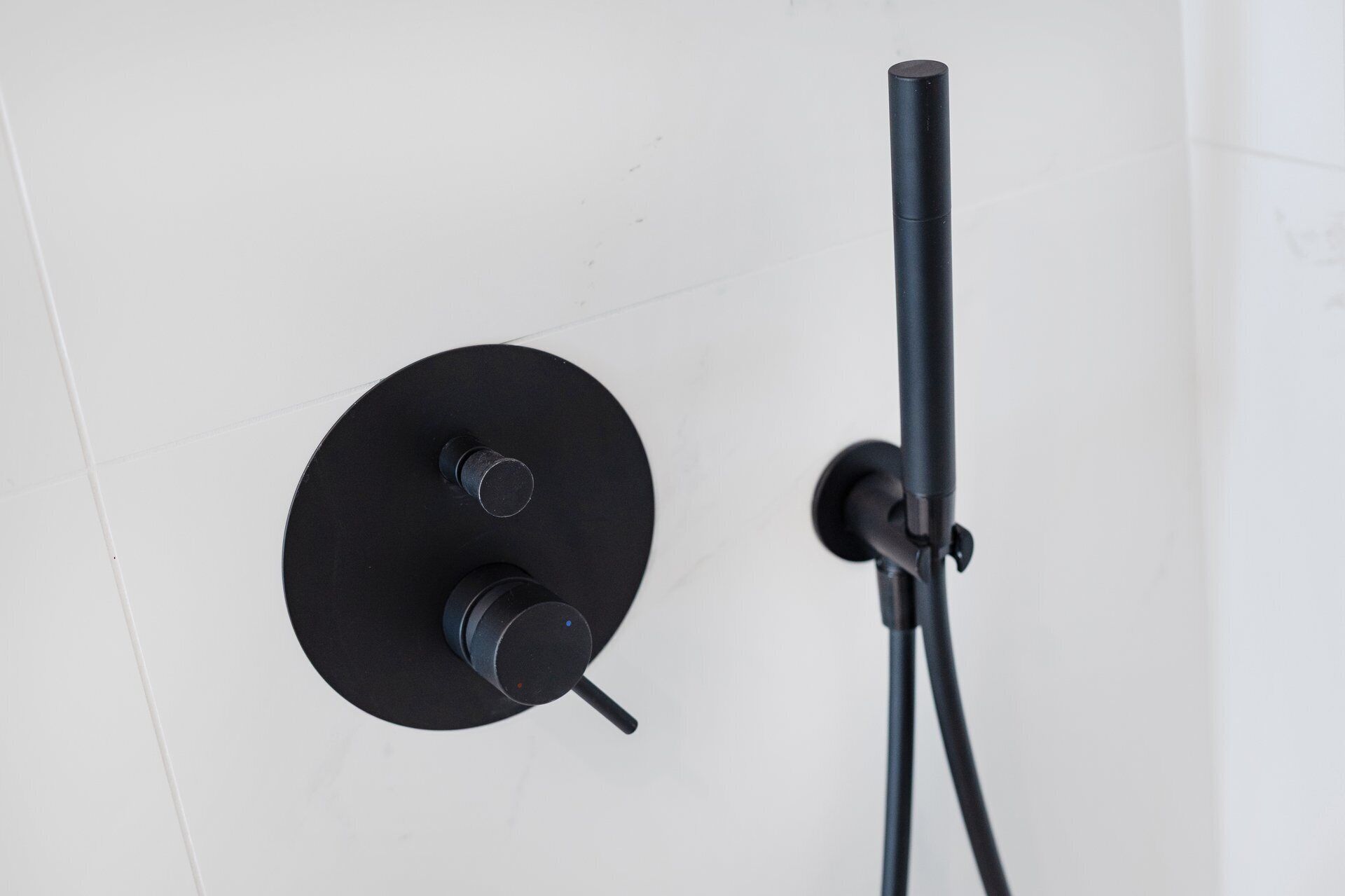 Une pomme de douche noire fixée sur un mur blanc.