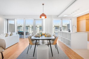 A modern apartment with a dining area, kitchen, and large windows. - Sal D'Ouro Ocean Views | Gym & Garage (Vila Nova de Gaia)