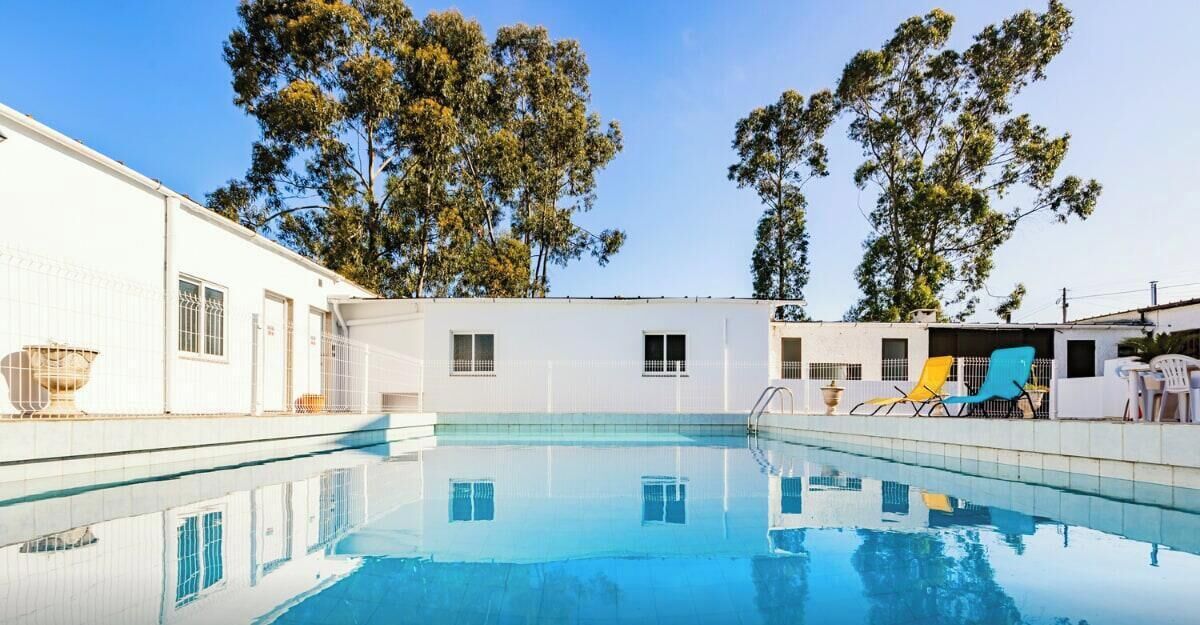 A swimming pool with a white building and trees in the background.