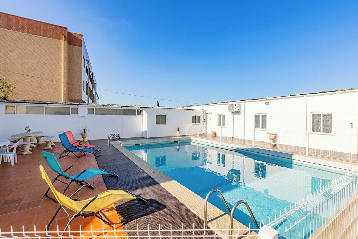 A rooftop swimming pool with lounge chairs, a table, and a building in the background.