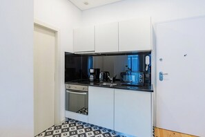 A compact kitchen with white cabinets, a black countertop, and a patterned floor. - Urban Studio @ Bonfim (Porto)