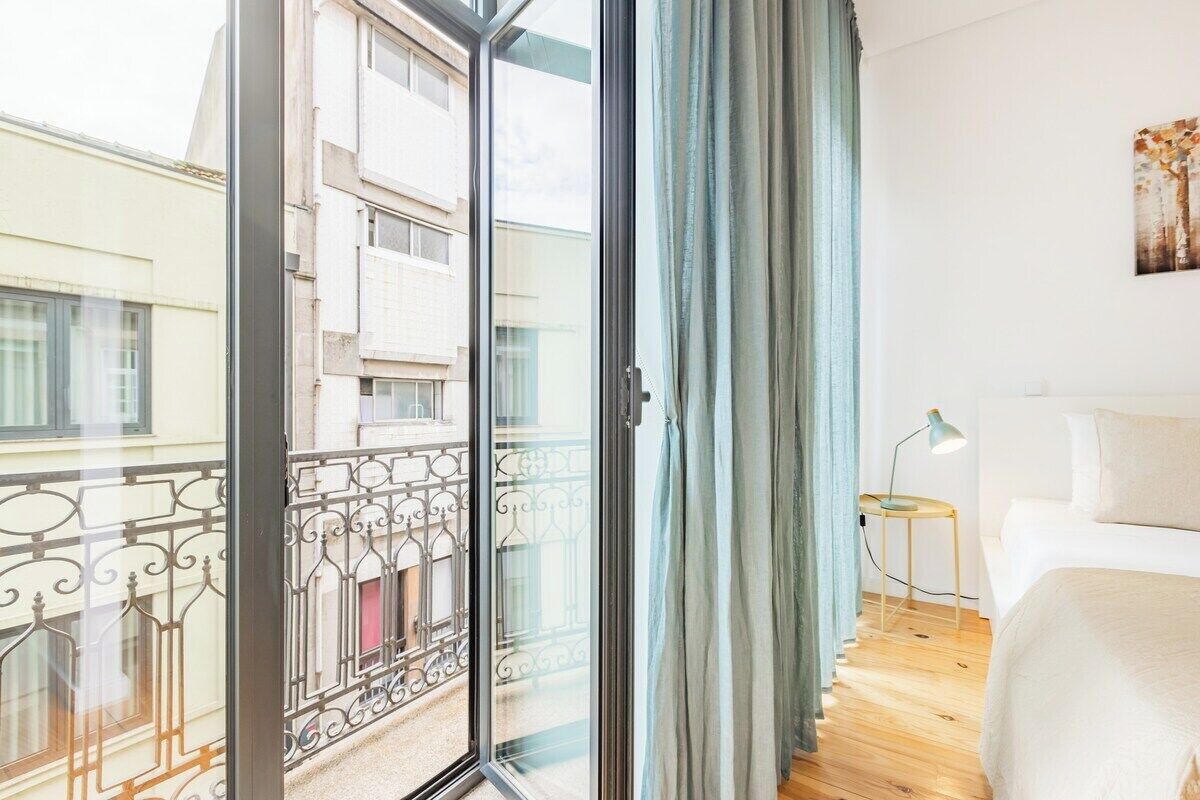 A bedroom with a large window, a bed, a nightstand, and a view of a building outside.