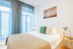 A hotel room with a bed, a nightstand, a lamp, a painting on the wall, and a window with curtains. - Urban Studio @ Bonfim (Porto)