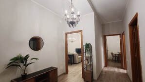 A hallway with a wooden floor, a mirror, a potted plant, a console table, a chandelier, and a plant shelf. - Cozy Apartment Overlooking the Main Square (Orsogna)
