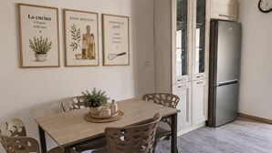 A modern kitchen with a dining table, chairs, a refrigerator, and three framed pictures on the wall. - Cozy Apartment Overlooking the Main Square (Orsogna)