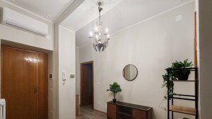 A hallway with a wooden door, a chandelier, a mirror, a potted plant, and a bookshelf. - Cozy Apartment Overlooking the Main Square (Orsogna)