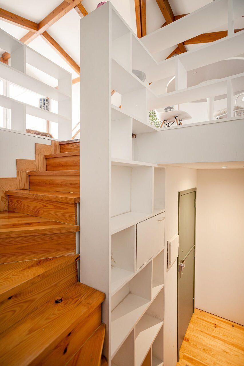 A wooden staircase leading to a white loft area with built-in shelving and a door.