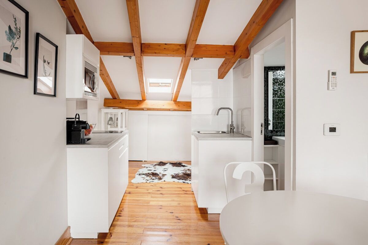 Una cocina moderna con armarios blancos, techo de madera y alfombra de cuero de vaca en el suelo.