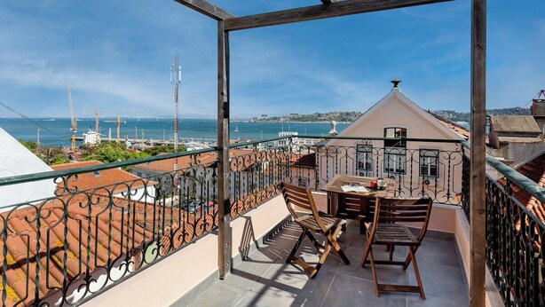 A balcony with a table and chairs, overlooking a coastal view with buildings and cranes. - Arriaga River Views II (Lisbon)