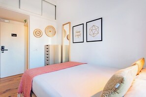 Hotellihuone, jossa on sänky, punainen heittopeitto, peili ja seinätaidetta, johon kuuluu geometrisiä kuvioita ja lause «Loista kirkkaasti».