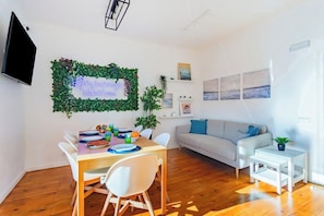 A modern living room with a dining area, a flat-screen TV mounted on the wall, a sofa, and a small white table with a plant. - Double Bedroom @ Guest Inn 1 Boutique House (campo pequeno)