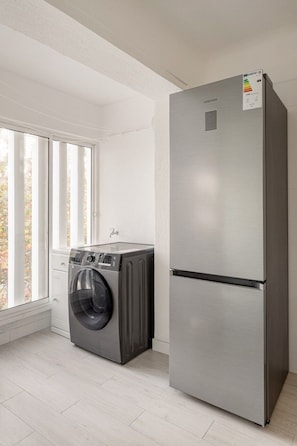 Eine kompakte Küche mit einem Edelstahl-Kühlschrank, einer eingebauten Waschmaschine und einem Fenster mit Jalousien.