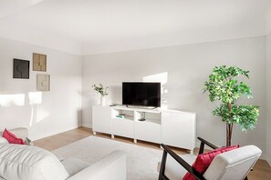 Ein modernes Wohnzimmer mit einem weißen Sofa, einem Flachbildfernseher auf einem weißen Schrank, einer Topfpflanze und Kunstwerken an der Wand.