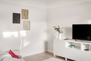 Een moderne woonkamer met een flatscreen televisie, witte meubels en wanddecoratie.