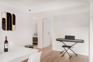 A modern room with a white table, a wine bottle, and glasses, a keyboard, and a bed in the background. - WFH Urban Retreat @ Carnide (Lisbon)