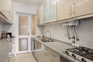 Een moderne keuken met granieten aanrechtbladen, roestvrijstalen apparatuur en licht houten kastjes.