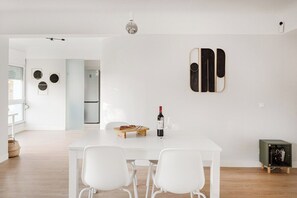 A modern kitchen with a white table, two white chairs, a wine bottle, and glasses on the table. - WFH Urban Retreat @ Carnide (Lisbon)