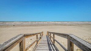 Un muelle de madera que lleva a una playa bajo un cielo azul despejado.