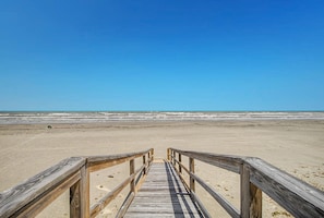 Ein hölzerner Steg führt zu einem Strand unter blauem Himmel.