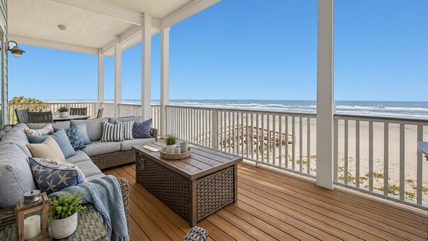 Un espacio al aire libre techado con una terraza de madera, un sofá con cojines, una mesita y vistas a la playa.