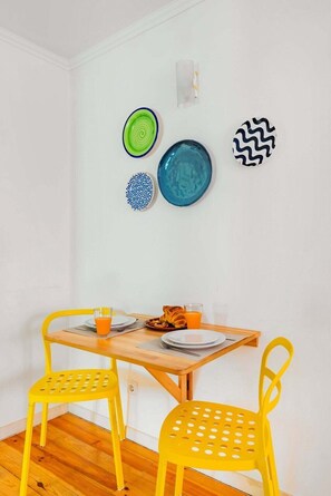 A dining area with a wooden table, yellow chairs, and colorful plates on the wall. - Alfama Comfy Studio (Lisbon)