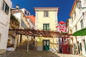 A narrow street with cobblestone pavement, a wooden pergola, and buildings with traditional architecture. - Alfama Comfy Studio (Lisbon)