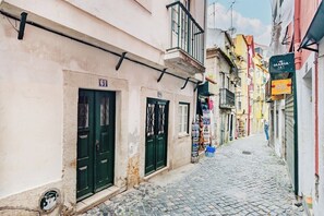 A narrow cobblestone street with buildings on either side, some with balconies and signage. - Alfama Comfy Studio (Lisbon)