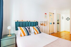 A bedroom with a bed, a nightstand, a lamp, a wardrobe, and a door leading to another room. - Alfama Comfy Studio (Lisbon)