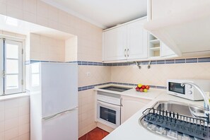 A kitchen with white cabinets, a stove, oven, microwave, and a sink with a dish rack. - Alfama Comfy Studio (Lisbon)