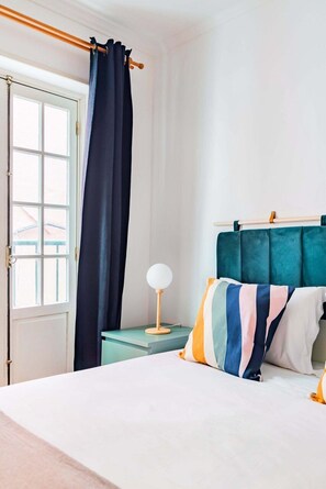 A bedroom with a bed, a bedside table with a lamp, a window with curtains, and a headboard. - Alfama Comfy Studio (Lisbon)