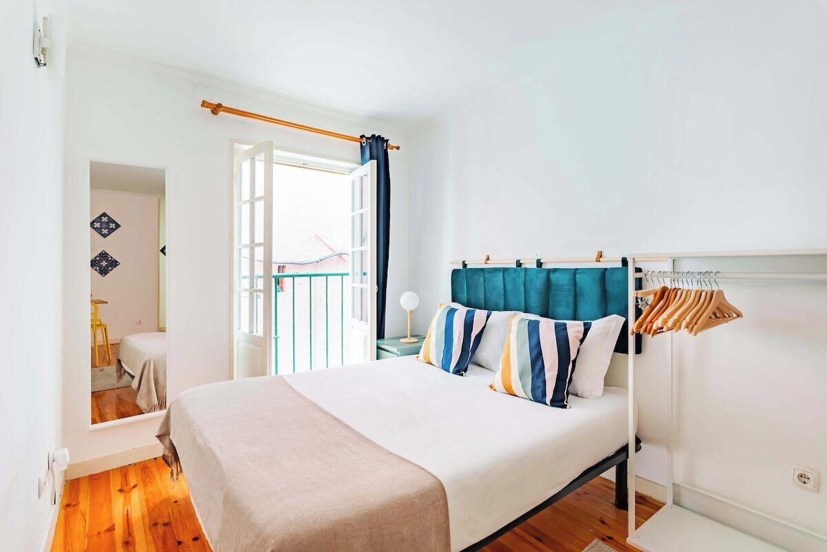 A bedroom with a bed, a window with curtains, a nightstand, and a clothing rack.