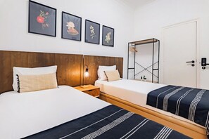 Quarto de hotel com duas camas, cabeceira de madeira, mesa de cabeceira com abajur e quadro com flores na parede.