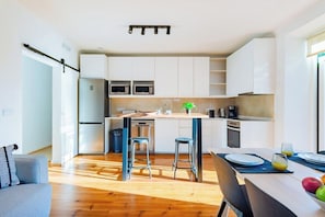A modern kitchen with white cabinets, stainless steel appliances, and a wooden dining table with bar stools. - Wood 'n' Touch Twin Room @ Guest Inn 2 (campo pequeno)