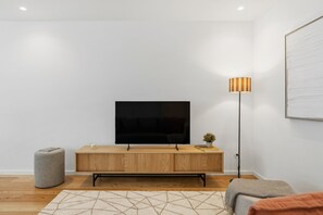 A modern living room with a flat-screen TV, a wooden cabinet, a floor lamp, and a patterned rug. - Sal D'Ouro | Terrace & Beach (Vila Nova de Gaia)