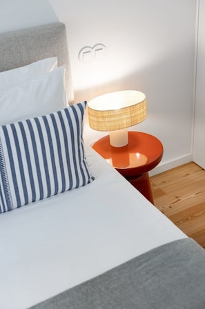 A bed with a striped pillow, a round orange nightstand with a lamp, and a wall with a circular design. - Sal D'Ouro | Terrace & Beach (Vila Nova de Gaia)
