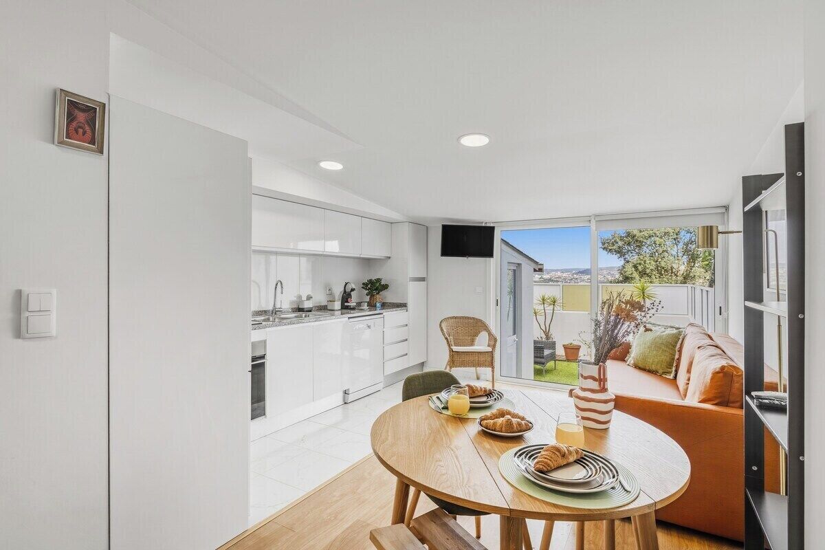 A modern kitchen with white cabinets, a dining table with breakfast items, and a sofa with a view to the outdoors.
