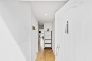 A hallway with white walls, a wooden floor, a white door, and a metal shelf with a picture frame. - Sunny House with Private Terrace | Gaia (Vila Nova de Gaia)