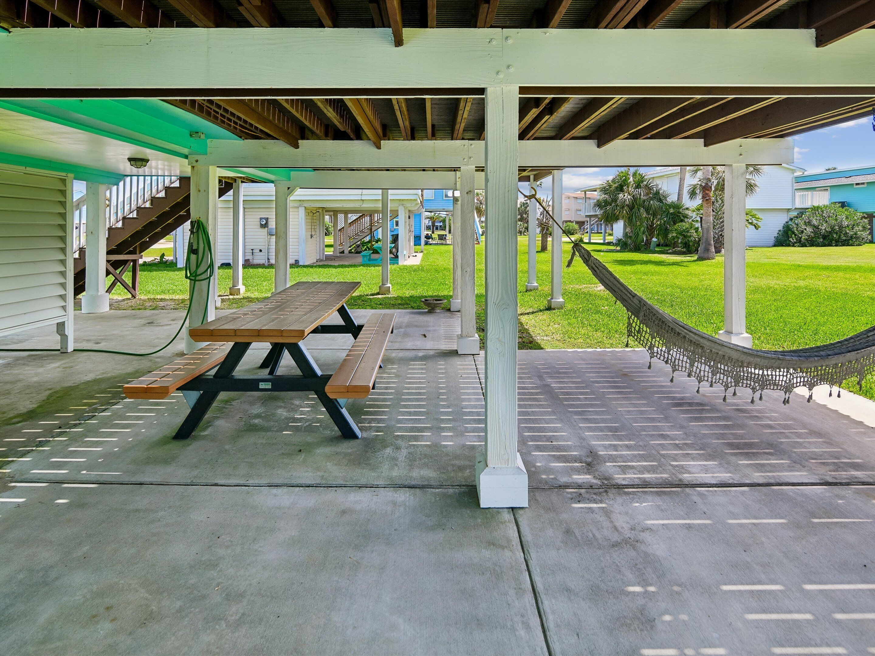 A covered outdoor area with picnic tables, a hammock, and a view of a residential area.