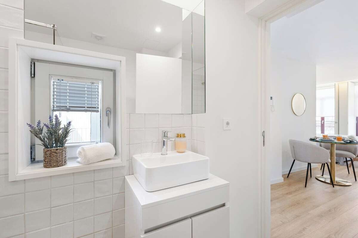 Een moderne badkamer met een witte wastafel, een spiegel en een raam met zonwering.