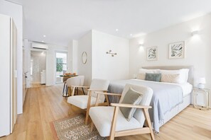 Ein modernes Schlafzimmer mit einem Bett, zwei Stühlen, einem kleinen Tisch und einem Nachttisch.