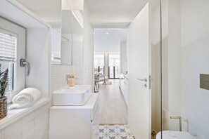Un baño moderno con un lavabo blanco, un espejo y un toallero.