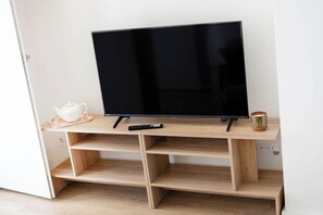 Ein Fernseher auf einem Holzständer mit Fernbedienung, einem Teekessel und einer Tasse auf dem Ständer.