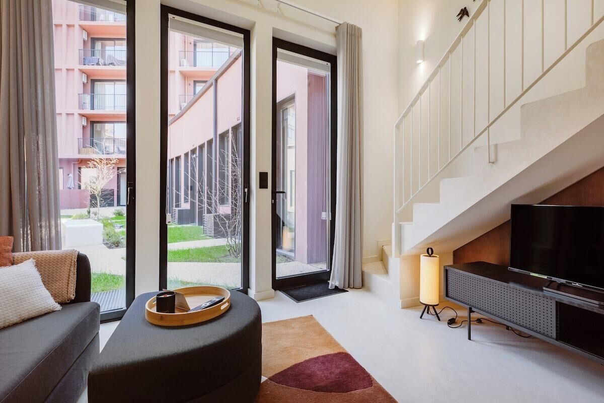 A modern living room with a sofa, a flat-screen TV, a coffee table, and a staircase.