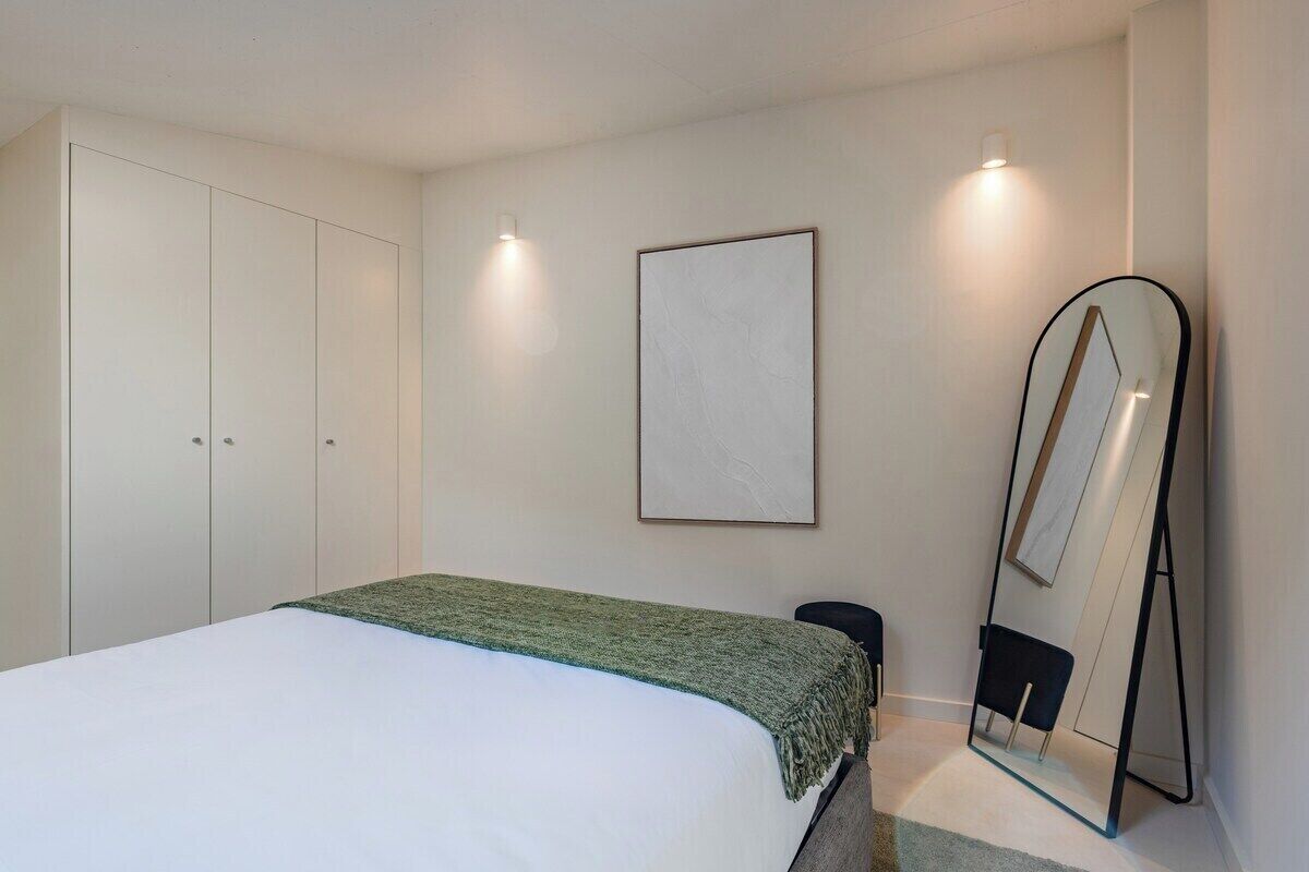 A bedroom with a bed, a wardrobe, a mirror, and a framed picture on the wall.