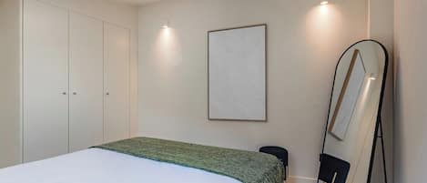 Un dormitorio con cama, armario, espejo y un cuadro en la pared.