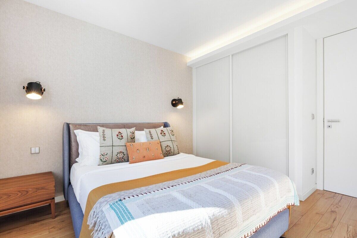 A bedroom with a bed, bedside tables, a wardrobe, and wall-mounted lights.