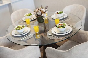 Une table ronde en verre, sur laquelle sont disposées quatre assiettes blanches, chacune contenant une salade et un verre de jus d’orange.