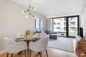 A modern living room with a glass dining table, grey sofas, and a large window with a city view. - Avenue 104 @ Porto Renovato, Bonfim (Porto)